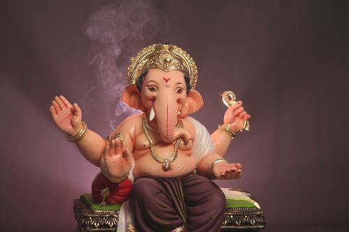 Free A detailed statue of Ganesha with decorative elements and incense smoke on a brown background. Stock Photo