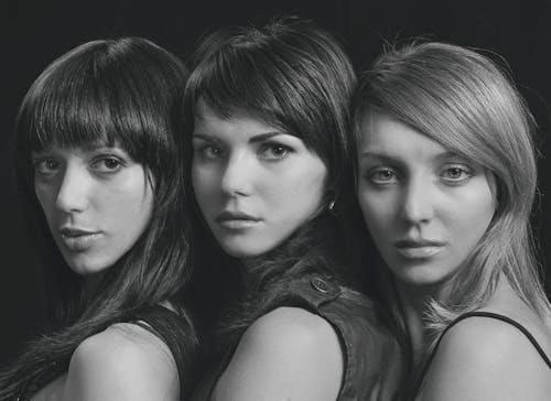 Grayscale Photography of Women Standing Beside Each Other while Seriously Looking at the Camera