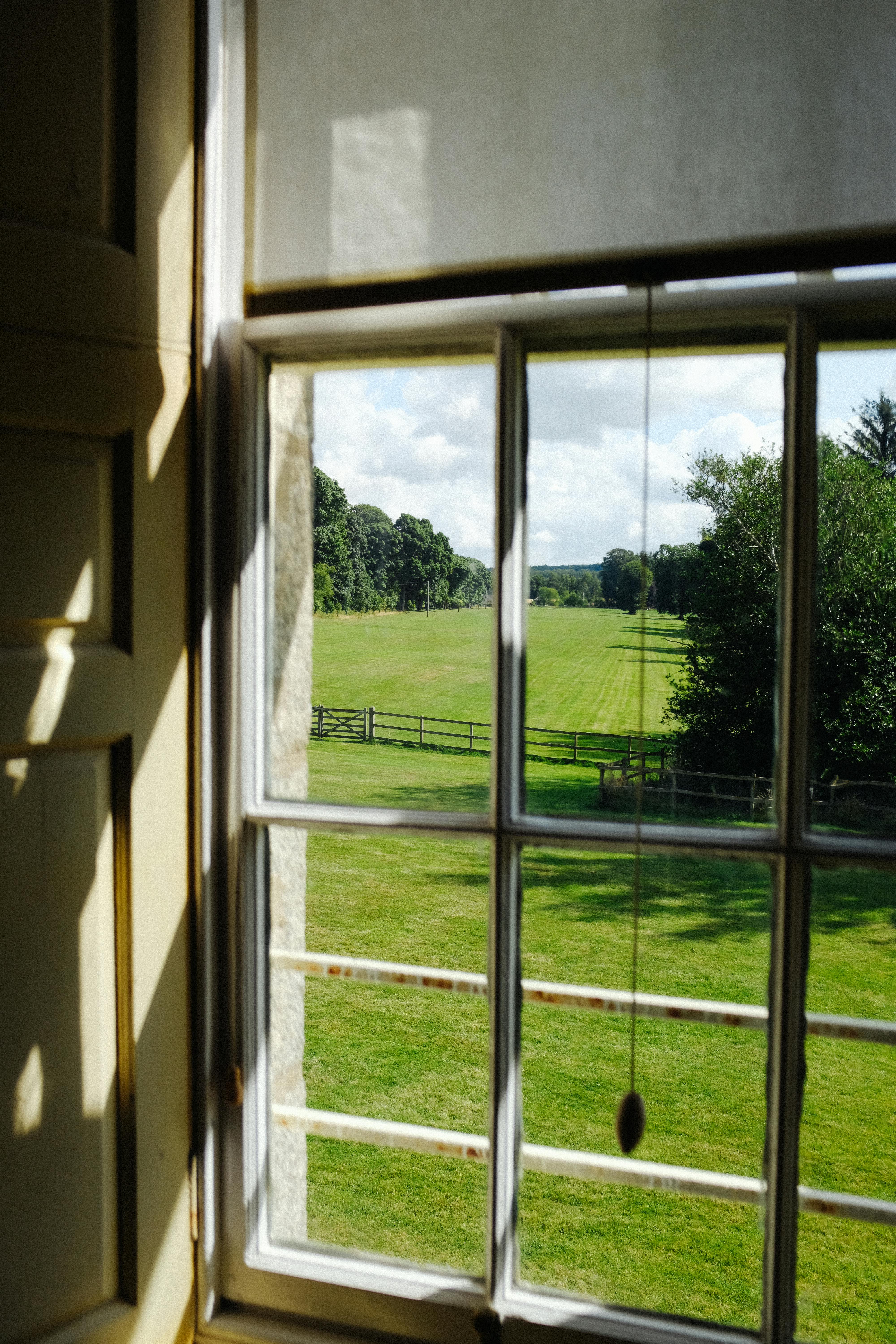 Beautiful countryside view through a window with lush green fields and trees.
