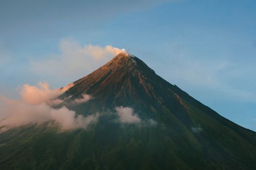 Free Stunning sunrise view of Mayon Volcano in Legazpi City, Bicol, with blue skies and steam rising. Stock Photo