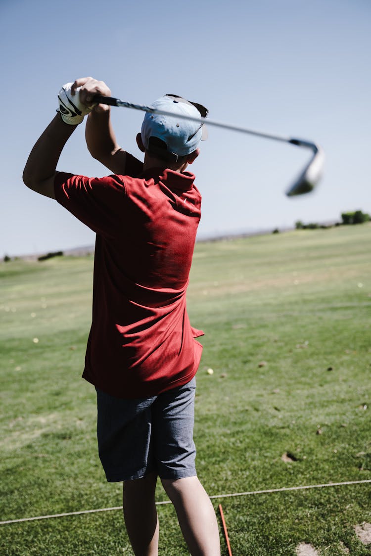 Man Swinging Golf Club Facing Grass Field