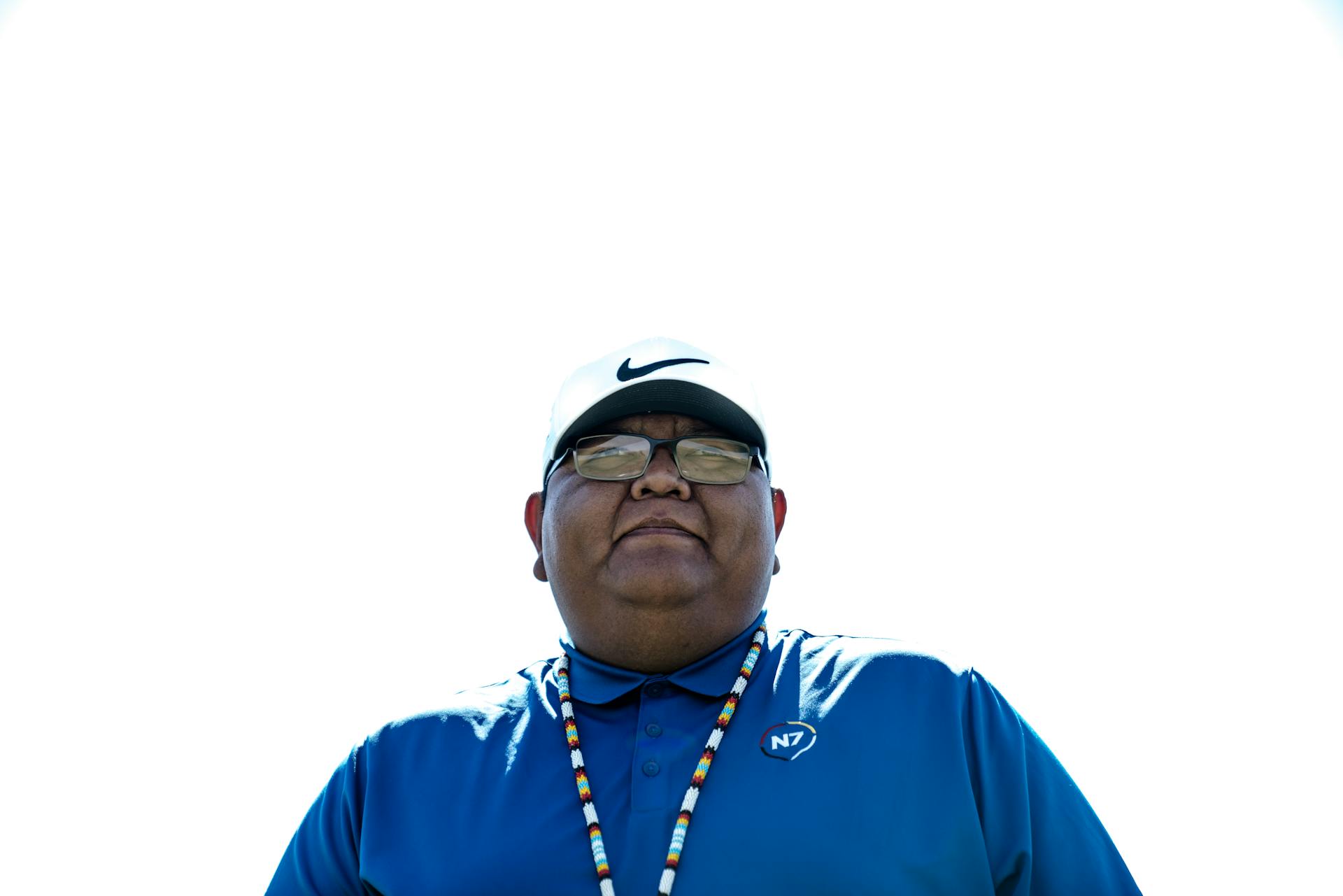 Low angle outdoor portrait of a man in a cap and blue shirt, under a bright sky.