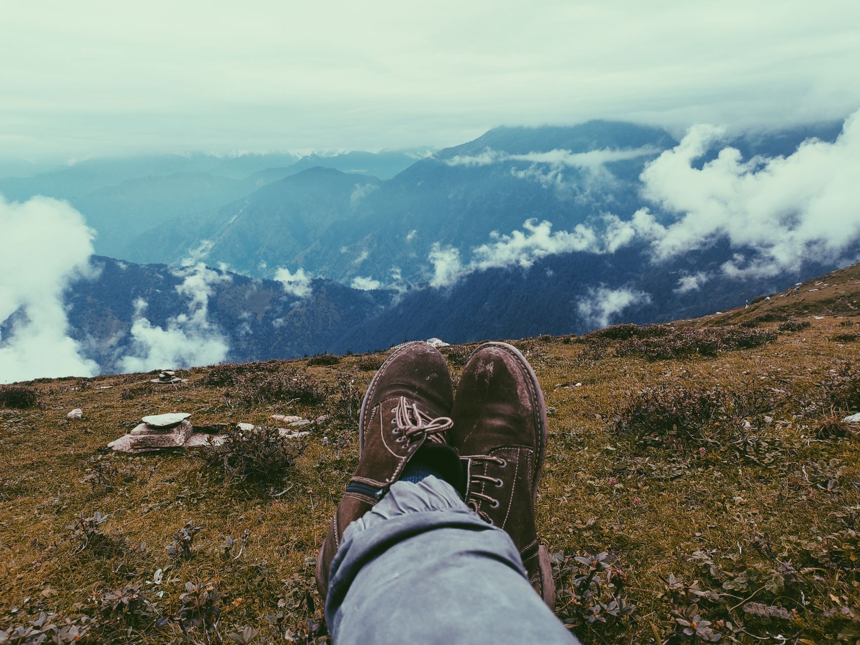 View from hilltop in Chopta, India with feet in foreground and clouds rolling over the Himalayan mountains.