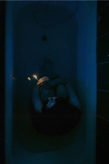 A woman sits in a bathtub at night, illuminated by a lighter. Dark and atmospheric.