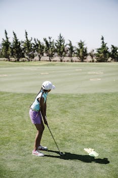 A child golfer prepares a swing on a sunny day on the golf course, showcasing youth sports.