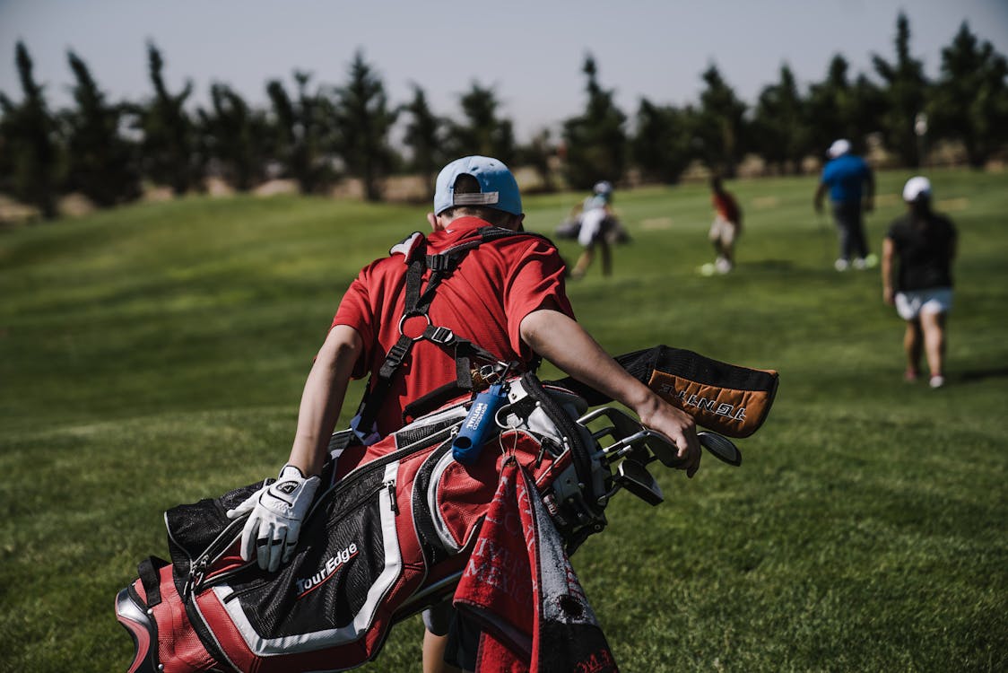 Mężczyzna Idący Niosący Czarny I Czerwony Torbę Golfową Na Polu Zielonej Trawie