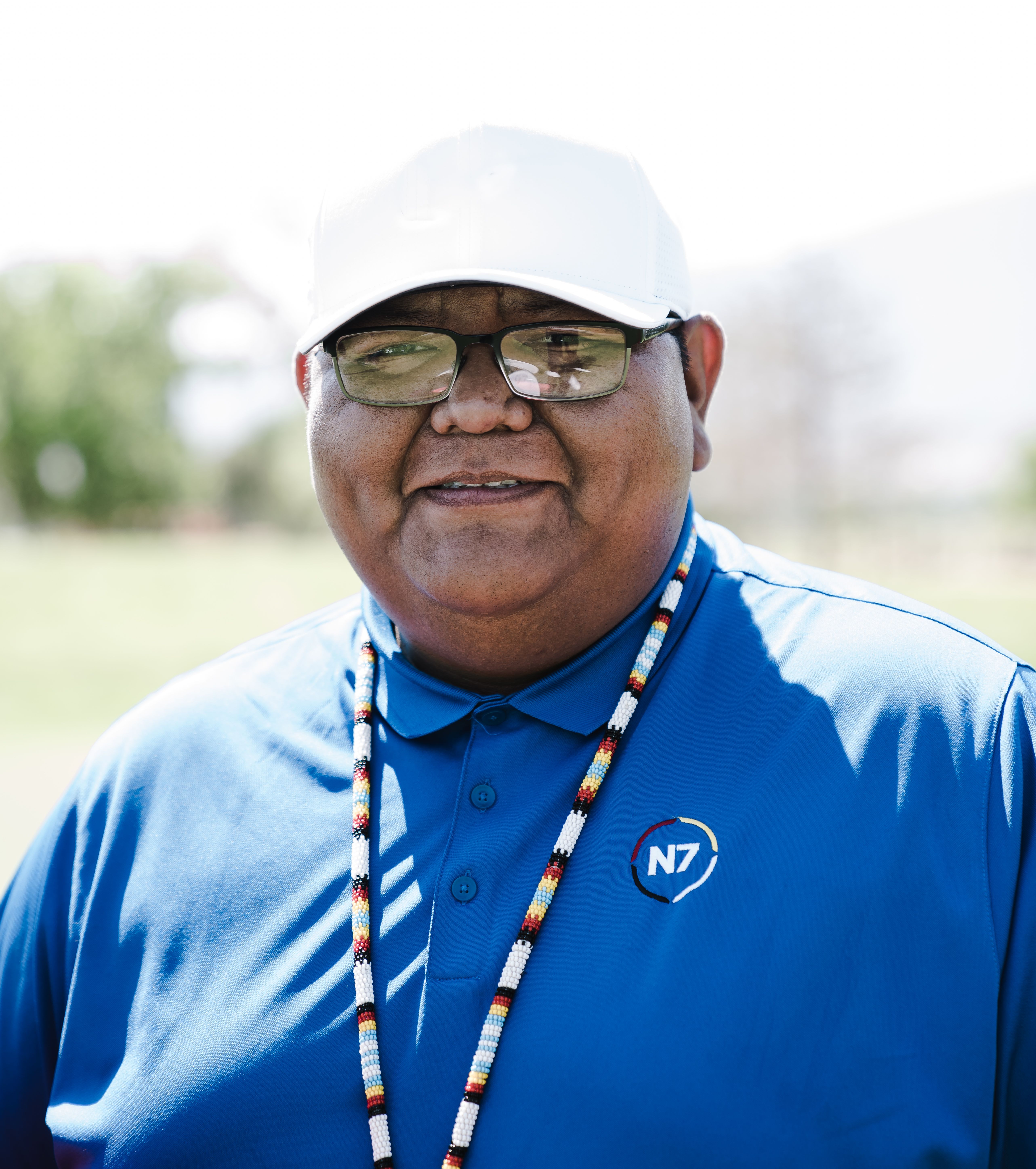 Portrait of a smiling man in a blue shirt and white cap, outdoors on a sunny day.