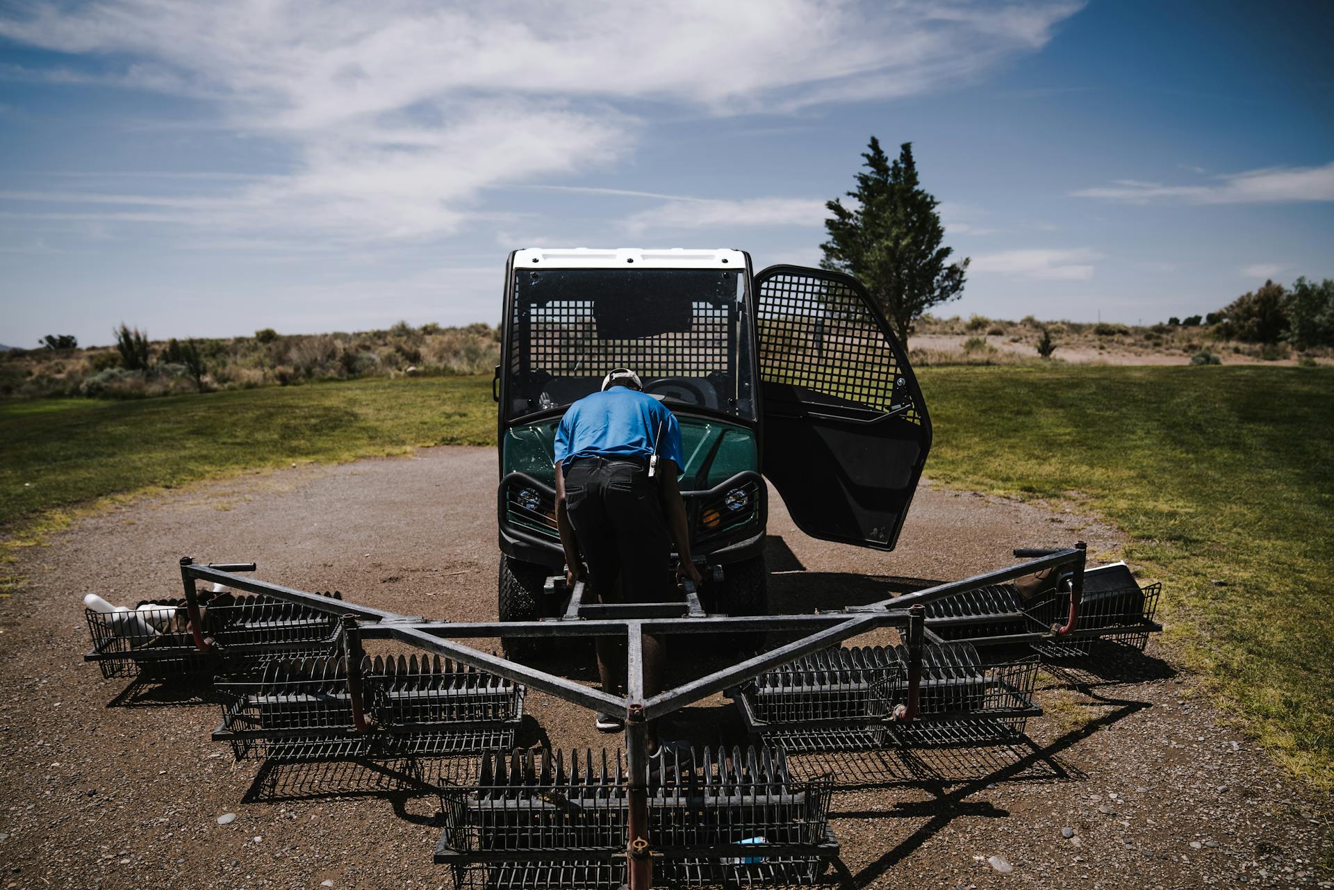 A worker maintaining golf course equipment with a tractor under clear skies.