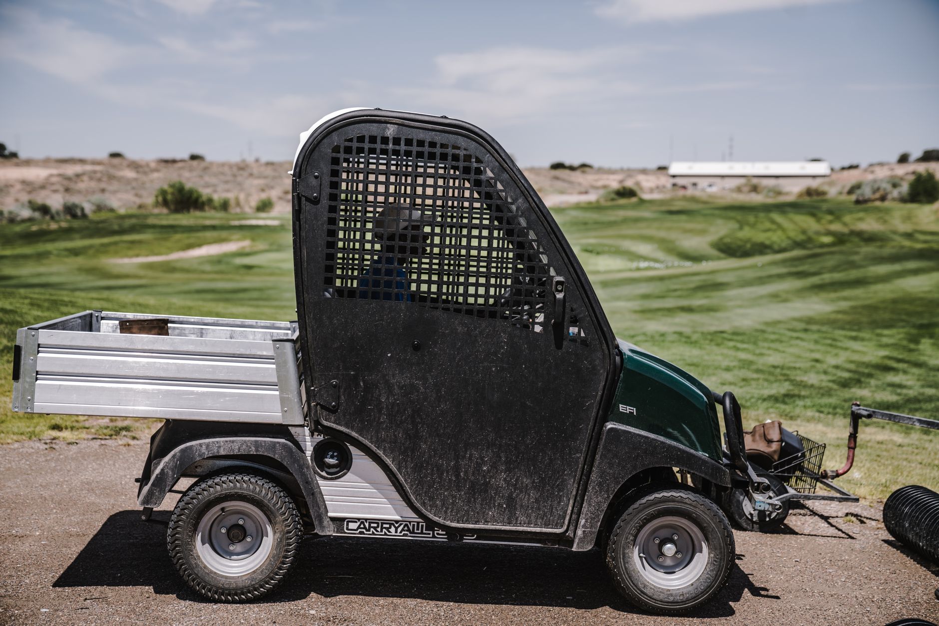 A utility vehicle parked outdoors at a sprawling golf course under a clear sky.