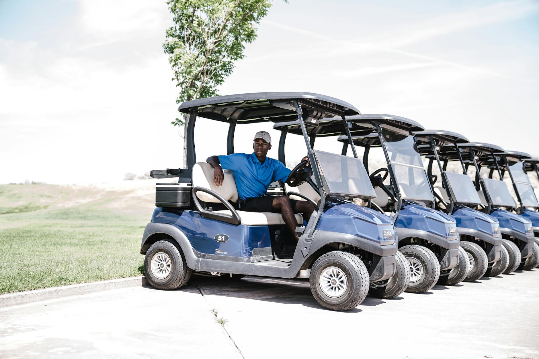 Man in Blue Shirt and Black Shorts Outfit Riding on Blue Golf Cart