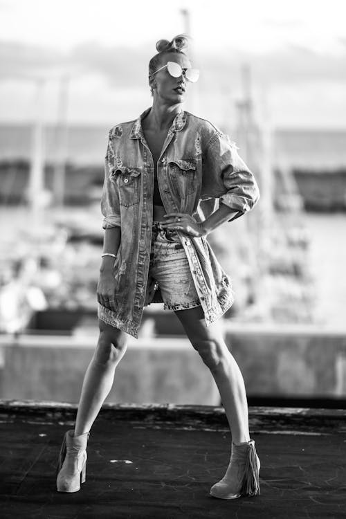 Grayscale Photo of Woman Posing While Wearing Denim Jacket and Denim Shorts 