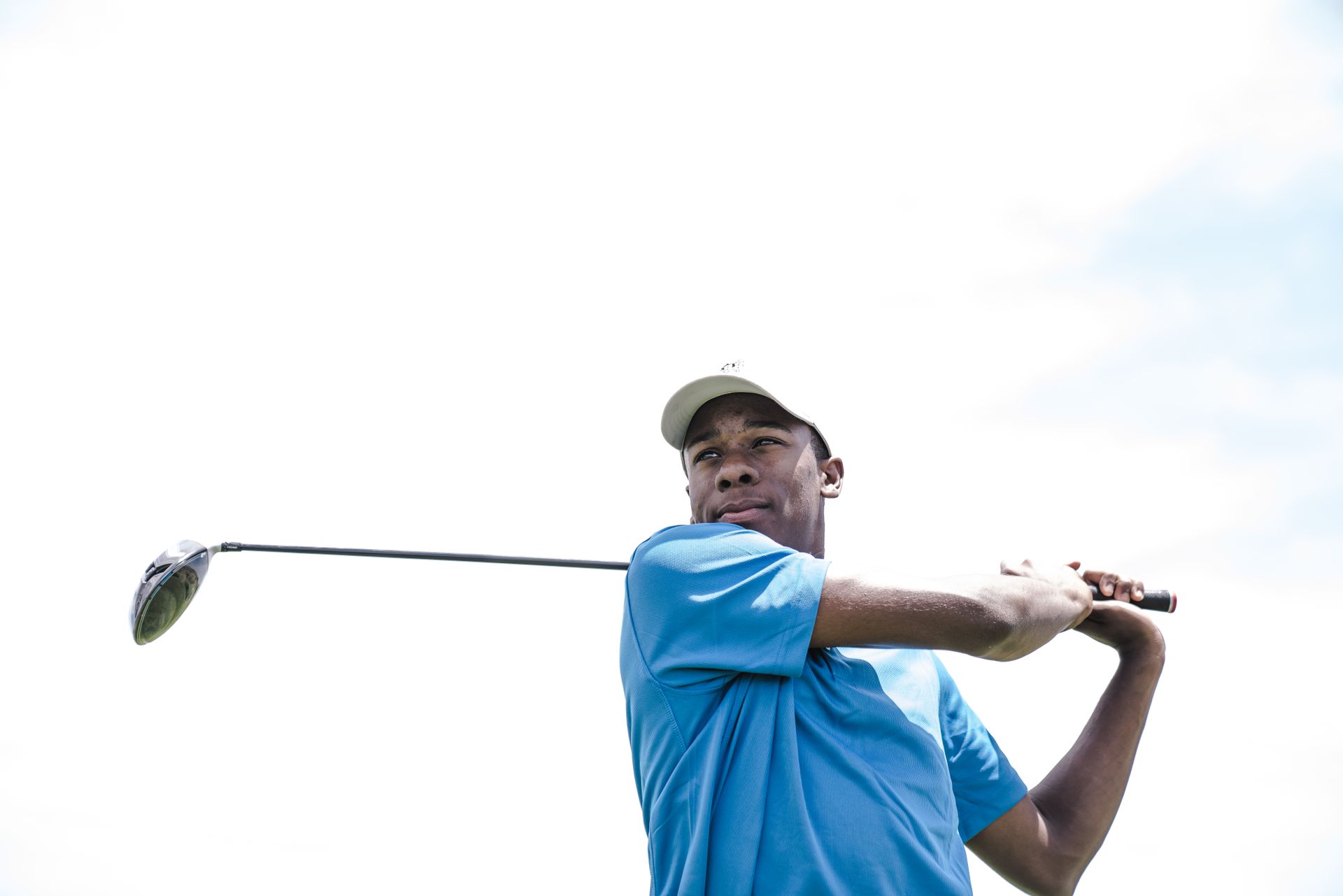 African American golfer mid-swing against a bright sky