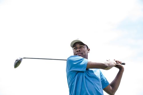 Free African American man playing golf against a bright sky, mid-swing. Stock Photo