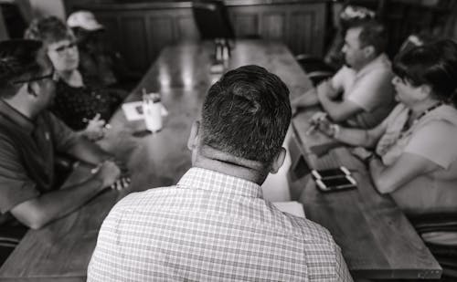 Foto Monocromática De Pessoas Perto De Uma Mesa De Madeira