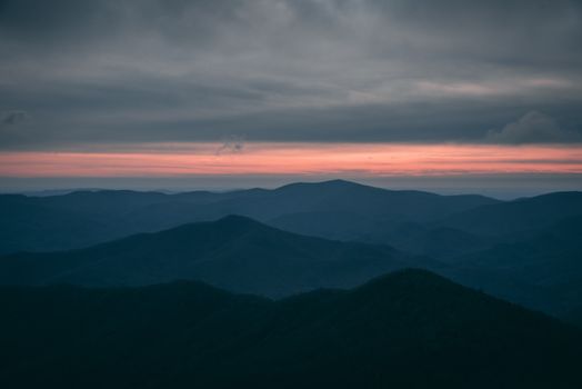 A breathtaking view of a rolling mountain landscape at twilight with a misty atmosphere and vibrant sky.