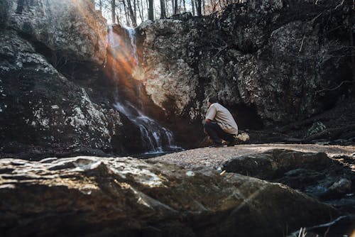 A Person Crouching near a Waterfall