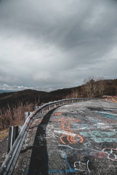 A winding road with colorful graffiti leading through lush hills under a cloudy sky.