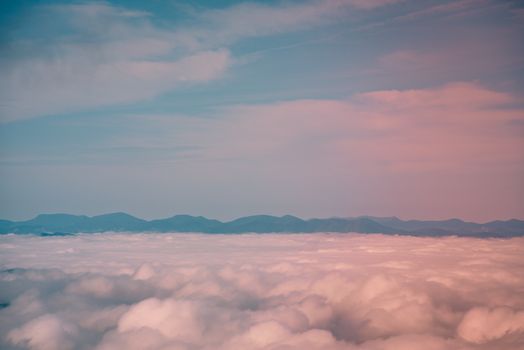 A tranquil aerial shot of soft, pink-tinted clouds with mountains in the distance.