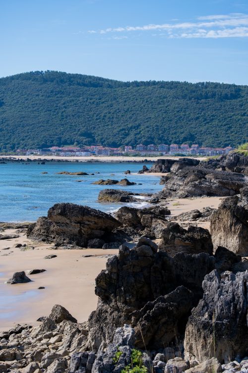 Free Explore the tranquil beauty of a rocky coastline under clear blue skies against a mountain backdrop. Stock Photo