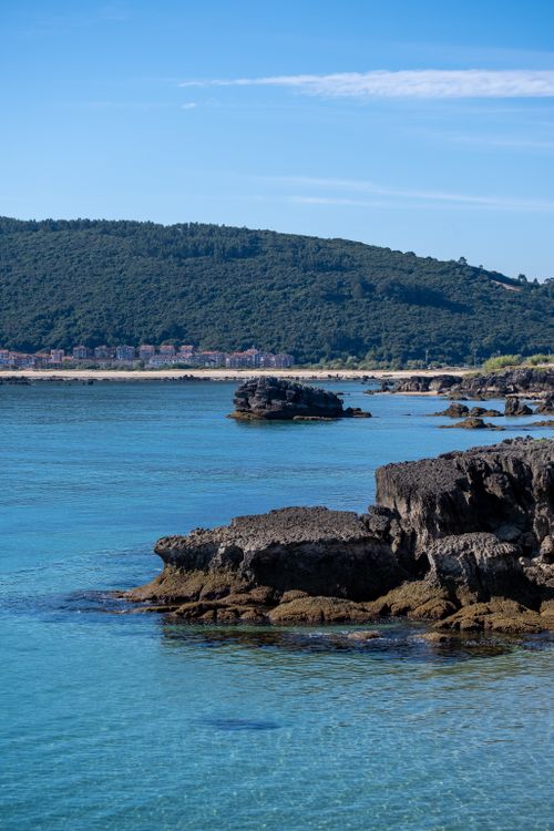 Free Scenic coastal view with rocky shoreline, clear blue waters, and lush green hills. Stock Photo