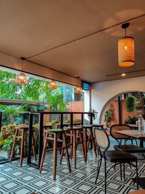 Free Cozy Bengaluru cafe with stylish wooden stools and lush green plants creating a warm ambiance. Stock Photo