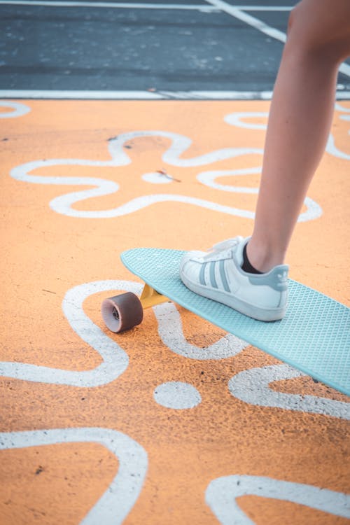 A Person Wearing White and Gray Shoe Stepping on Light Blue Skateboard