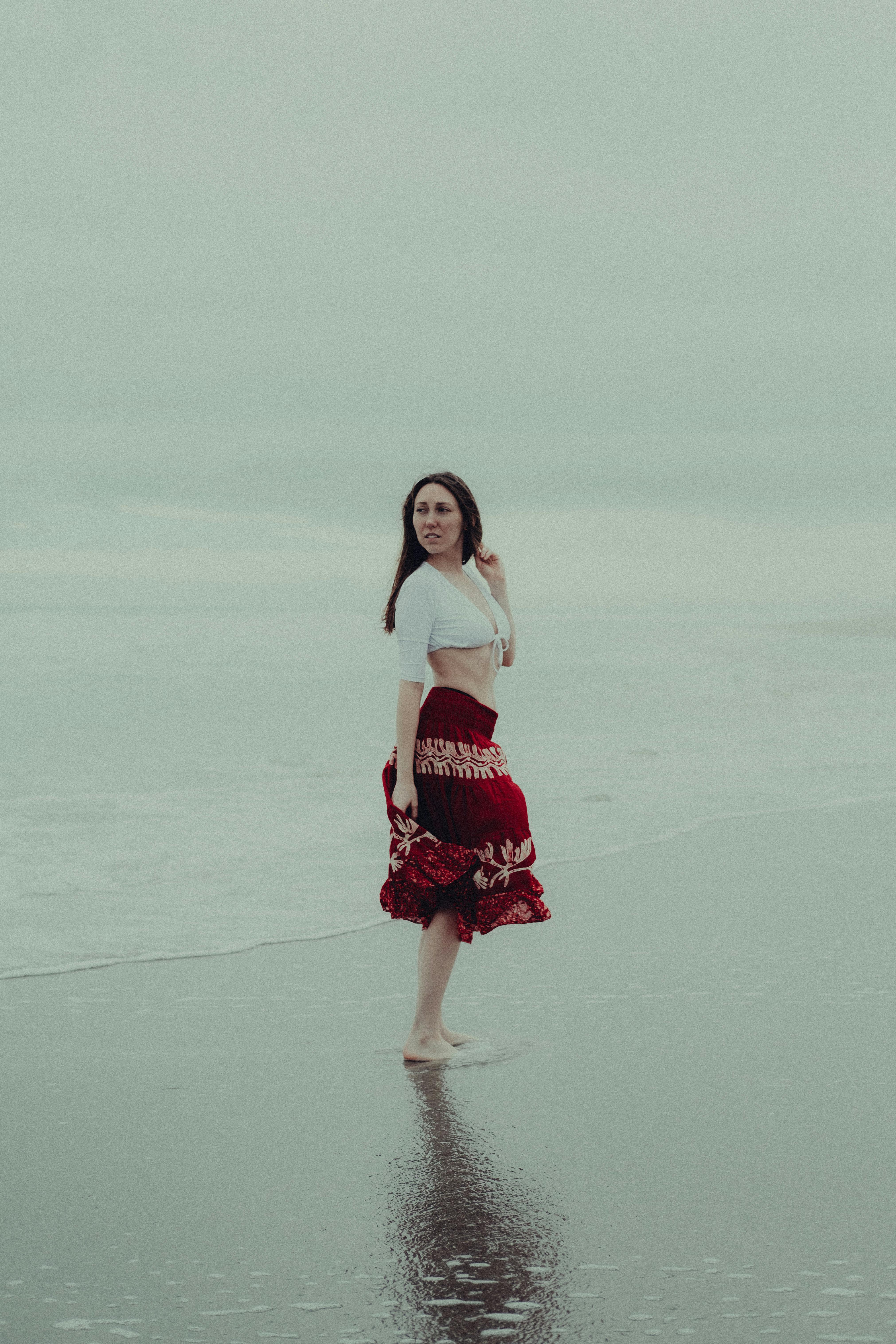 woman in white crop top and red floral skirt standing on beach