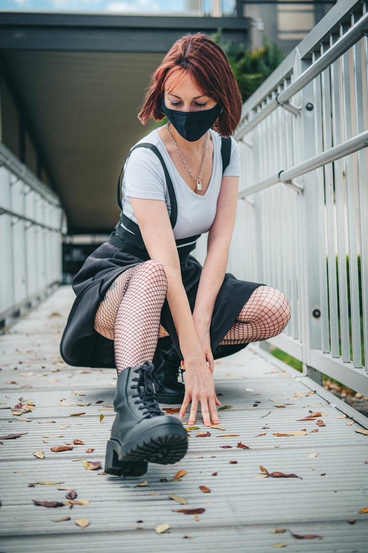 Woman In White Shirt And Black Skirt Squatting On Metal Bridge