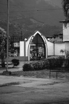 Monochrome image of a gothic-style cemetery gate in Mérida, Venezuela, with Andes mountains in the backdrop.