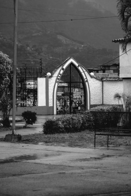 Fotomural Imagen en blanco y negro de una puerta de cementerio de estilo gótico en Mérida, Venezuela, con las montañas de los Andes de fondo.