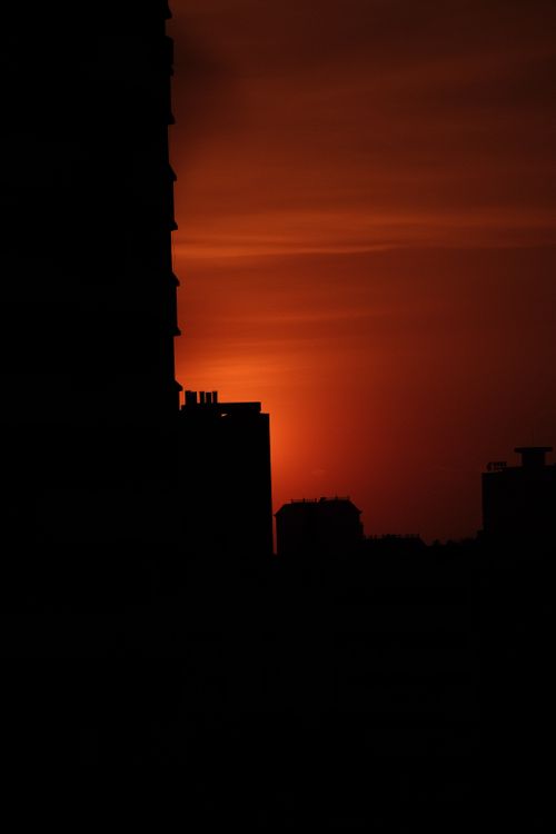 Free Dramatic silhouette of city buildings highlighted by an intense orange sunset sky. Stock Photo