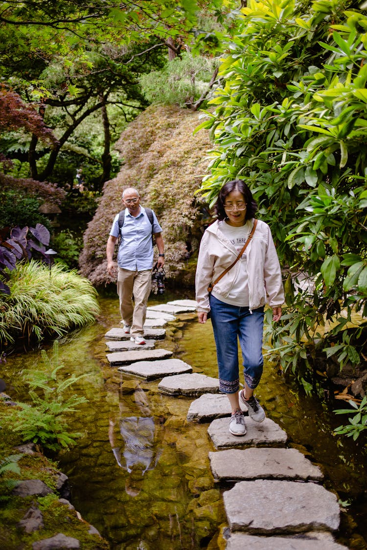 Woman And Man Walking On Stones On Pond In Park