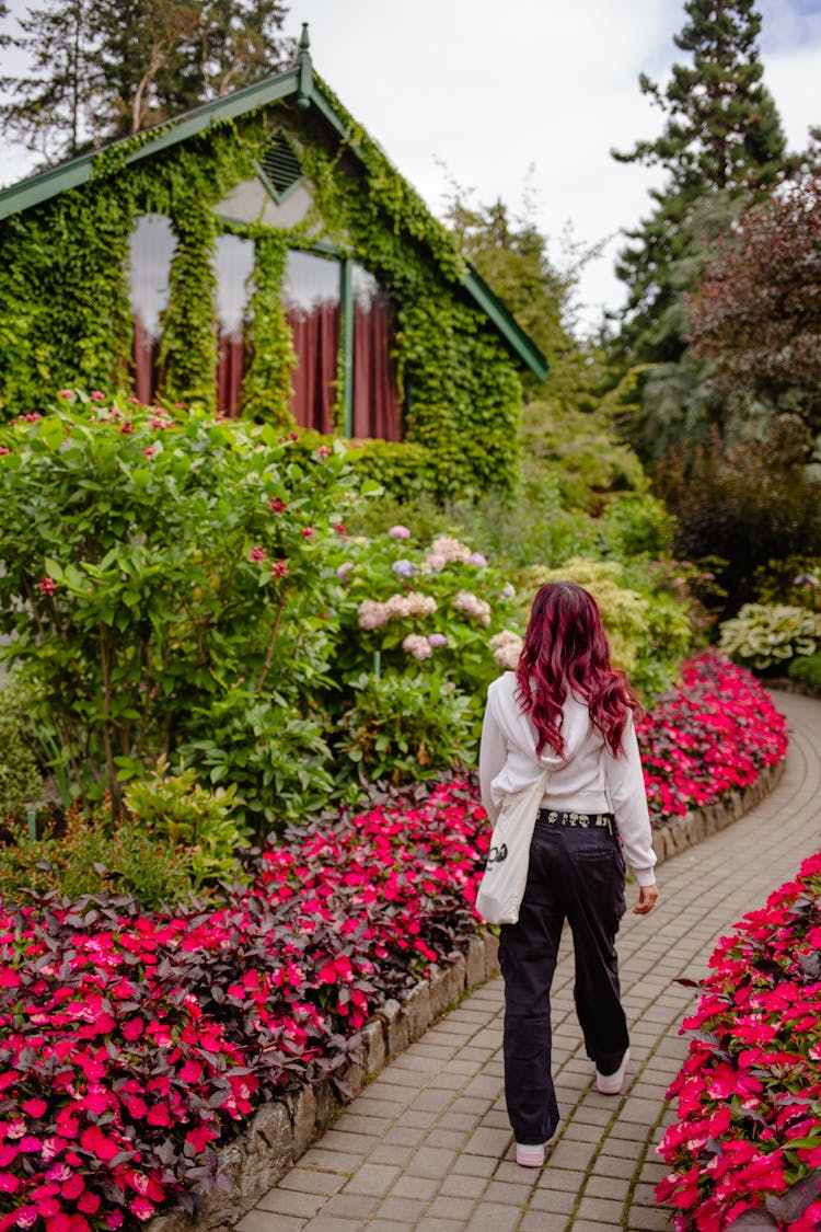 Woman Walking Near House With Colorful Flowers Around