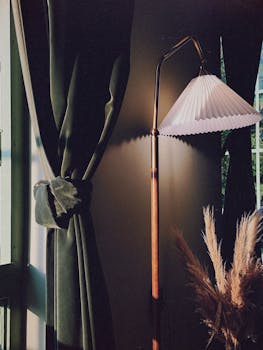 Elegant living room corner featuring a vintage lamp, dark green curtains, and pampas grass.