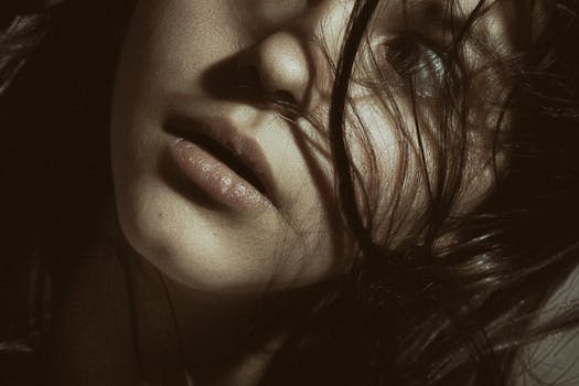 A dramatic close-up portrait of a woman with hair gently blowing across her face, creating intriguing shadows.
