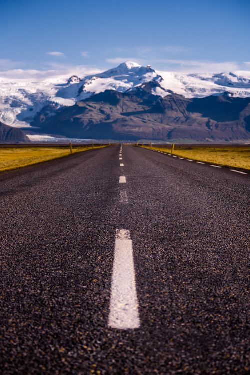 Free A captivating view of a road stretching towards snow-capped mountains in Iceland, perfect for travel inspiration. Stock Photo