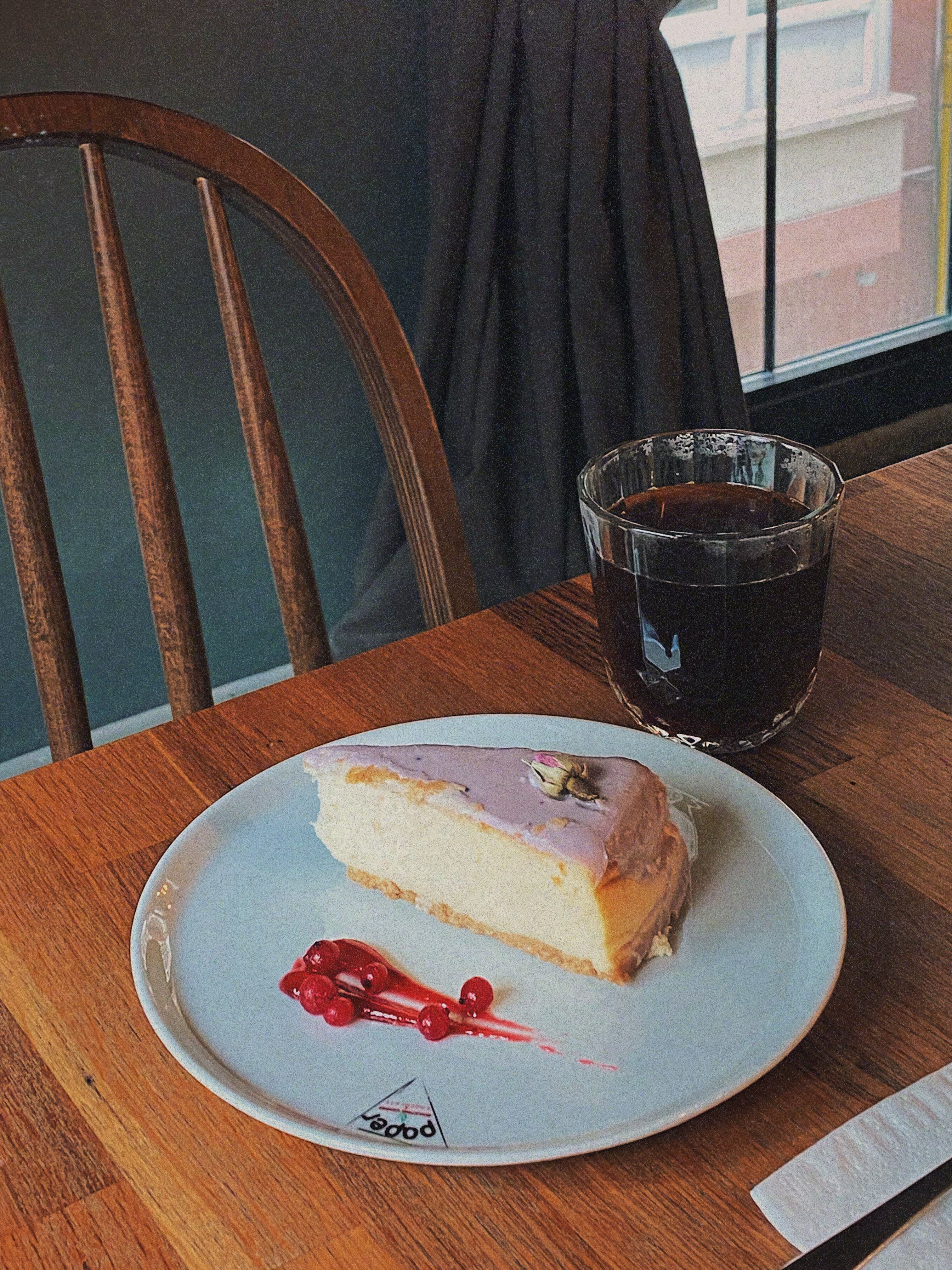 A slice of cheesecake with berries and coffee in a cozy café setting.