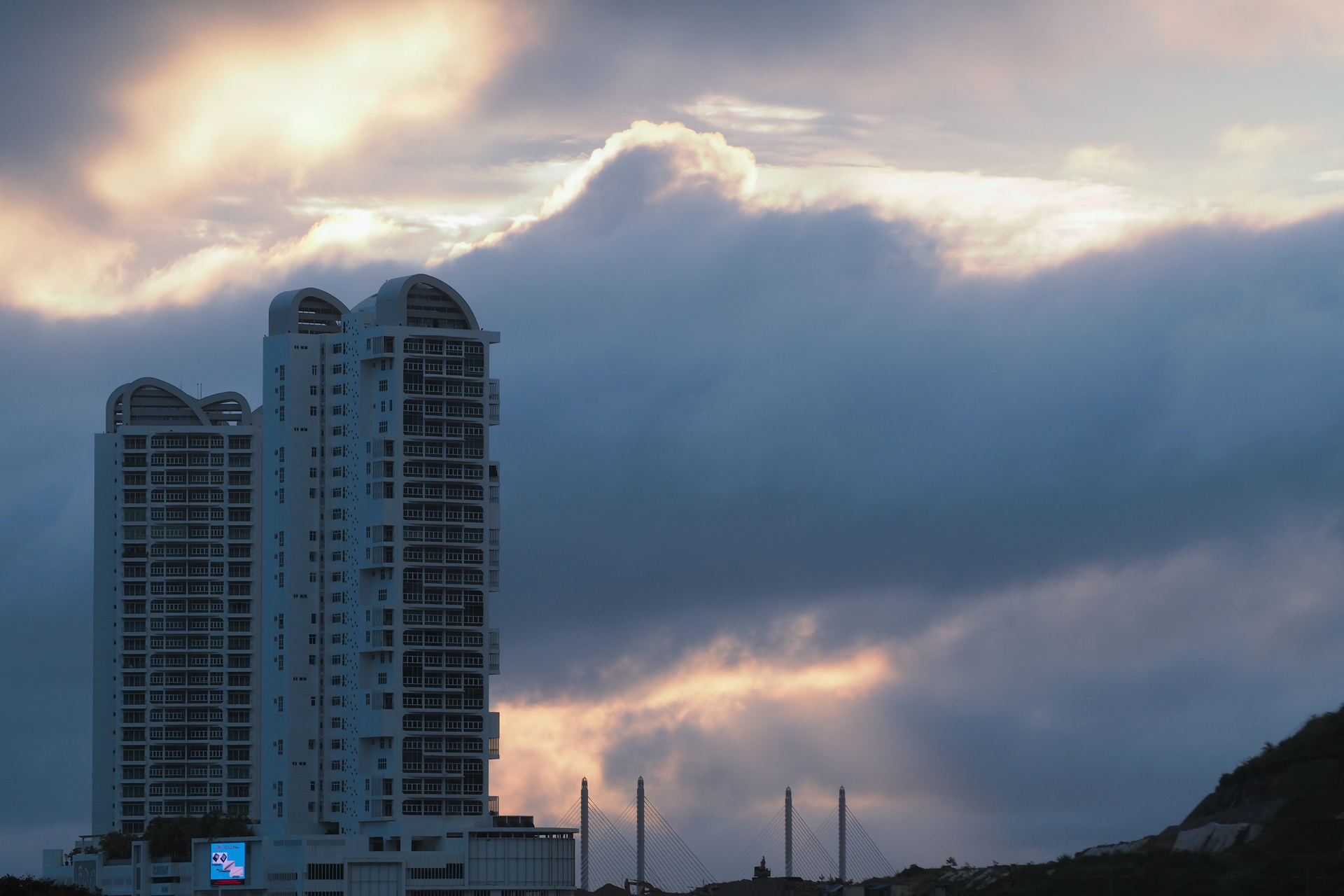 Two high-rise buildings silhouette against a dramatic cloudy sky during twilight.