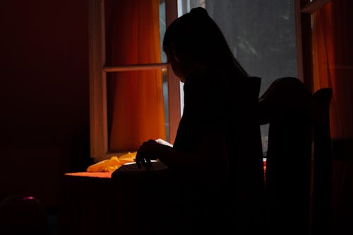 Silhouette of a Woman Sitting at a Table in the Evening 
