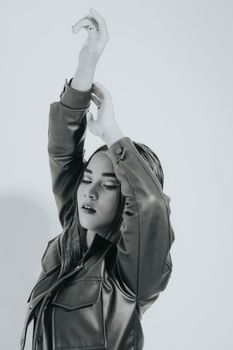 A young woman elegantly poses while wearing a leather jacket in a monochrome setting.