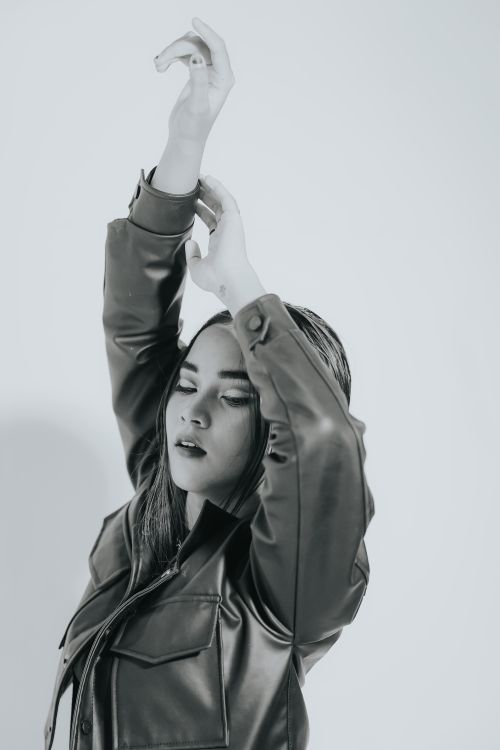 Free A young woman elegantly poses while wearing a leather jacket in a monochrome setting. Stock Photo