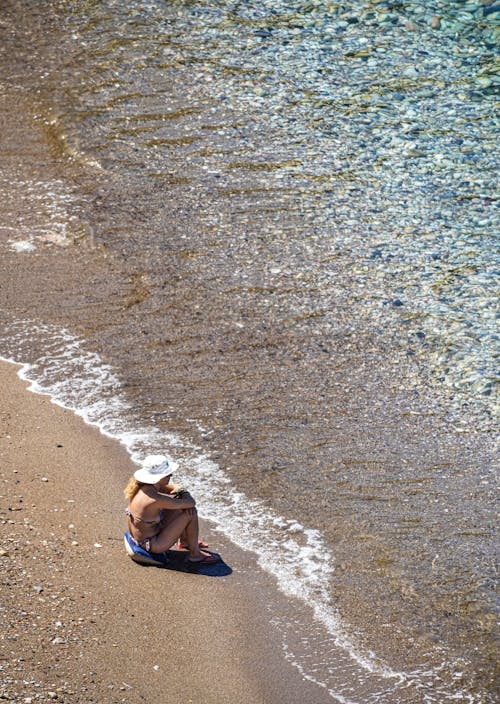 Person Alone Sitting on Seashore in Bikini Top and Sun Hat