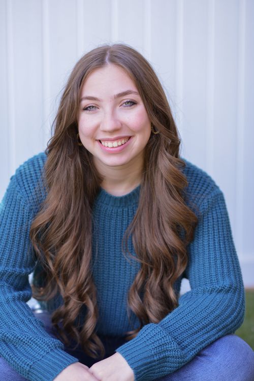 Free Portrait of a young Caucasian woman with long hair smiling and sitting indoors in a blue sweater. Stock Photo