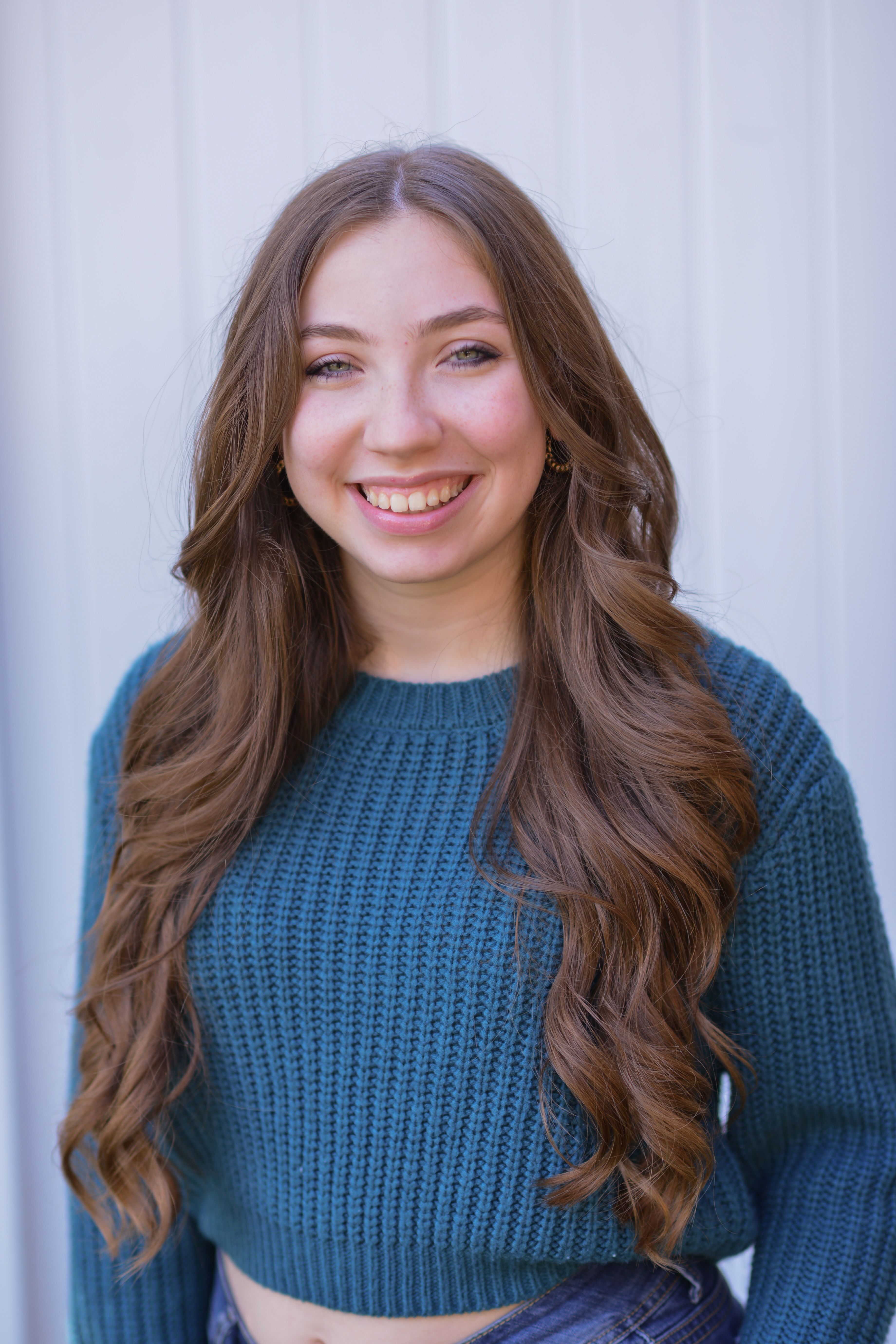 A cheerful young woman in a blue knitted sweater smiling at the camera against a white background.