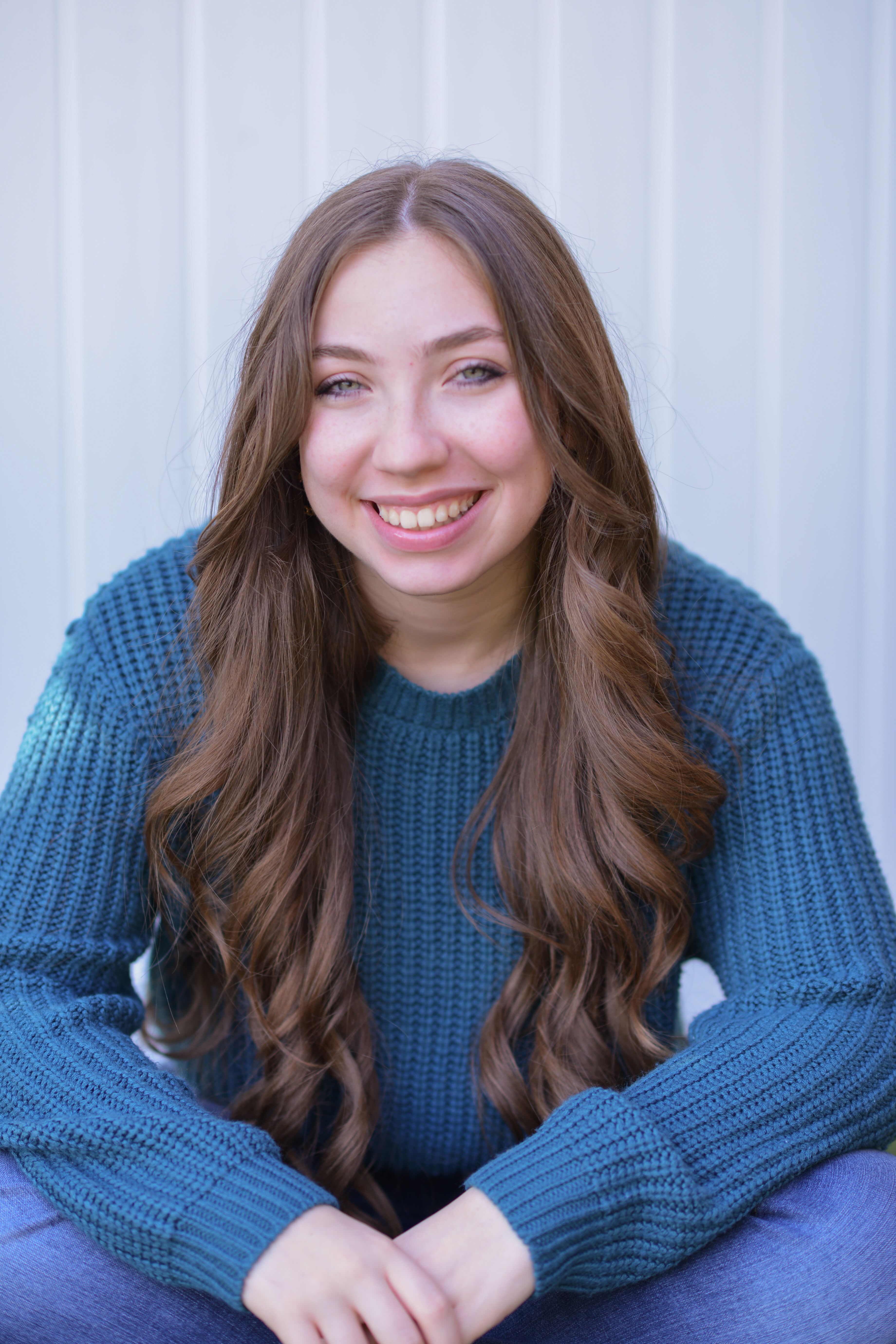Charming portrait of a young woman wearing a blue sweater, sitting and smiling.