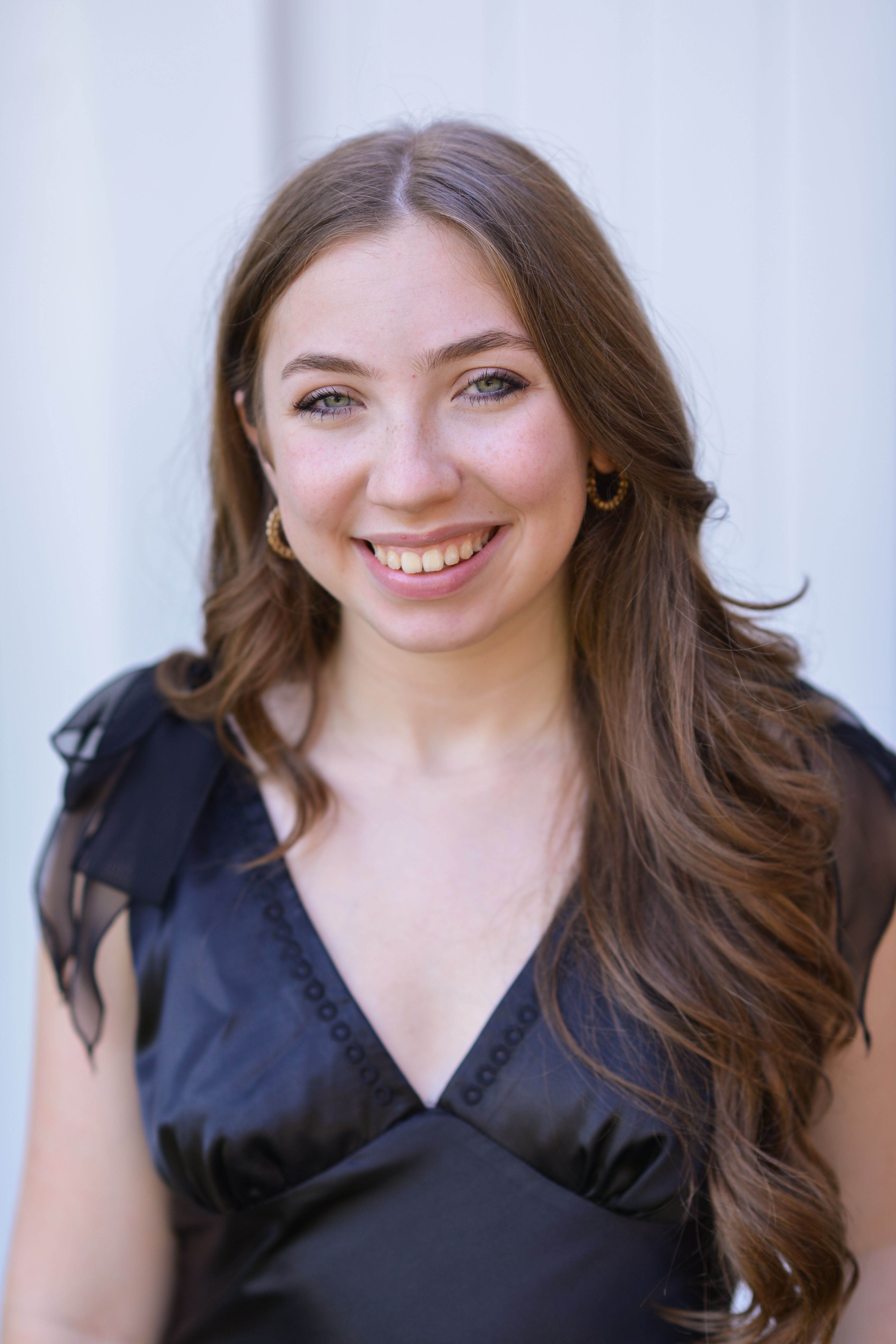 Portrait of a smiling young woman in a stylish black dress with long brown hair.