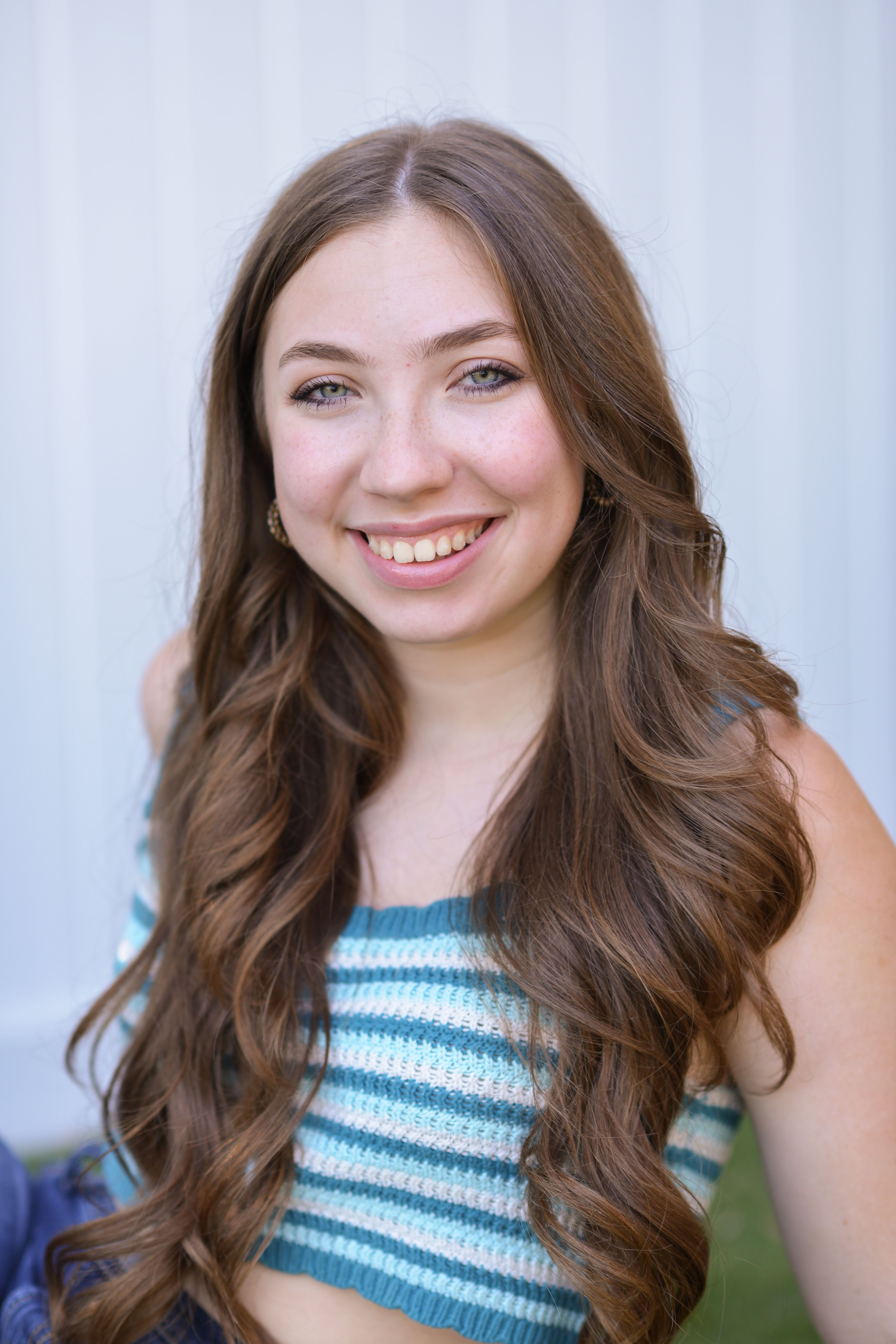 A young woman with long hair and a crochet top smiling outdoors.