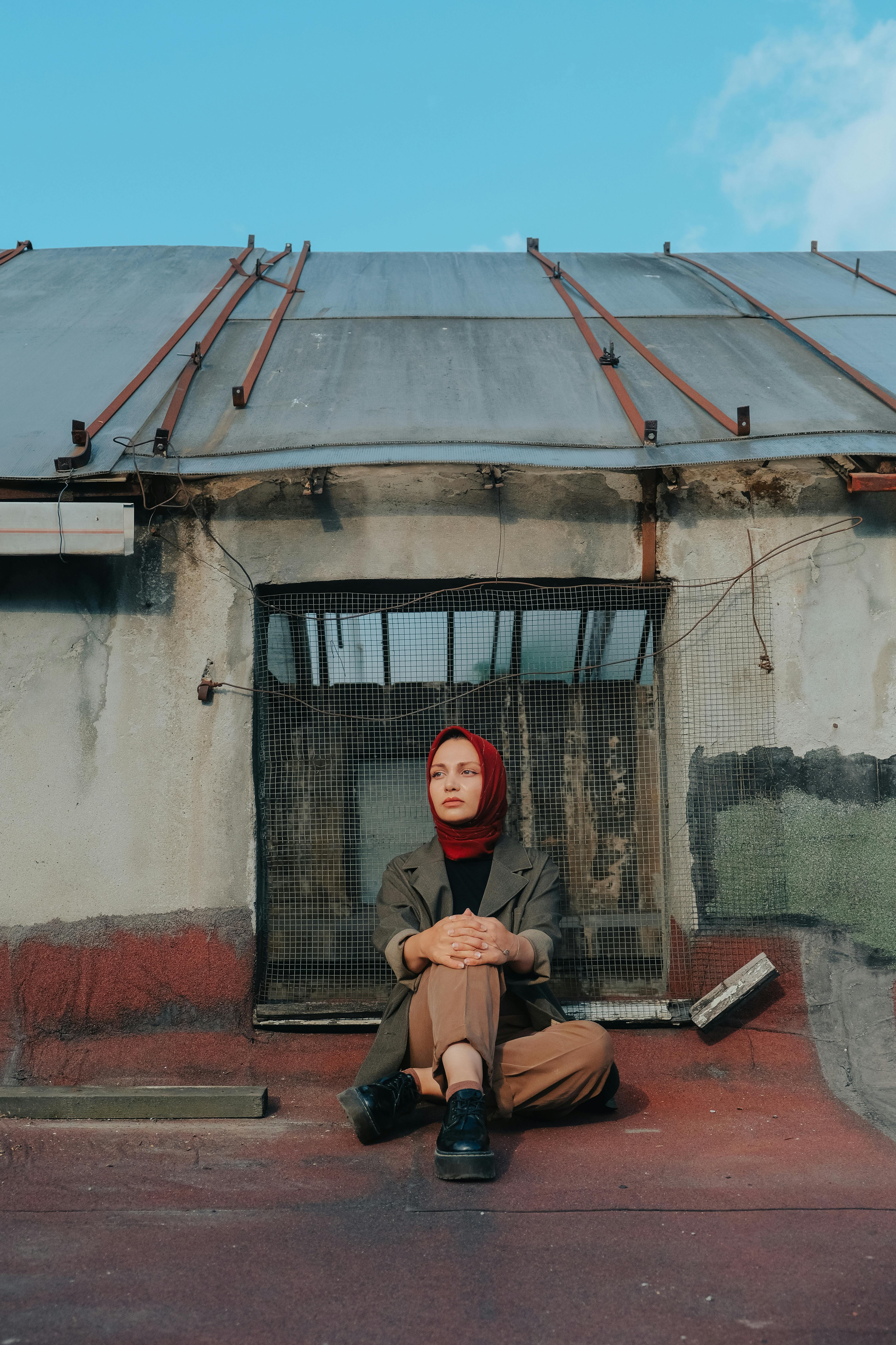 A woman in a hijab sits thoughtfully on a rooftop, against an urban backdrop.