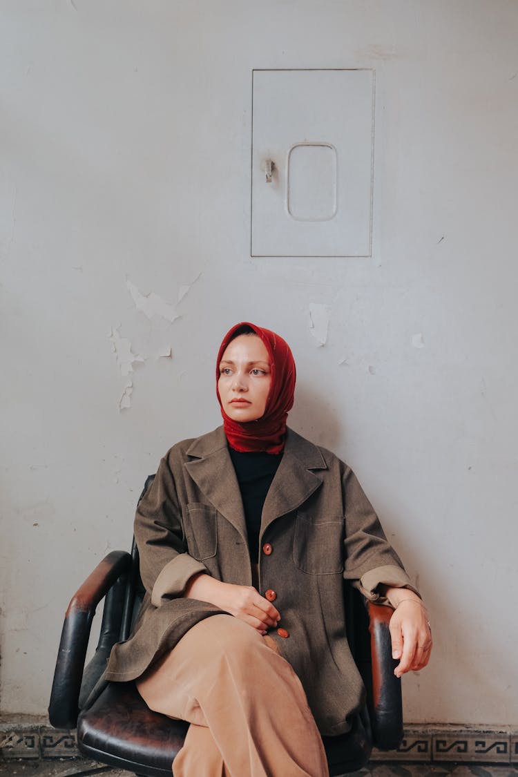 Woman In Hijab Sitting In Office Chair Near White Wall