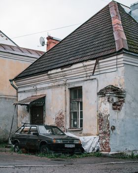 A vintage car parked outside an old, weathered house with peeling paint and crumbling bricks.
